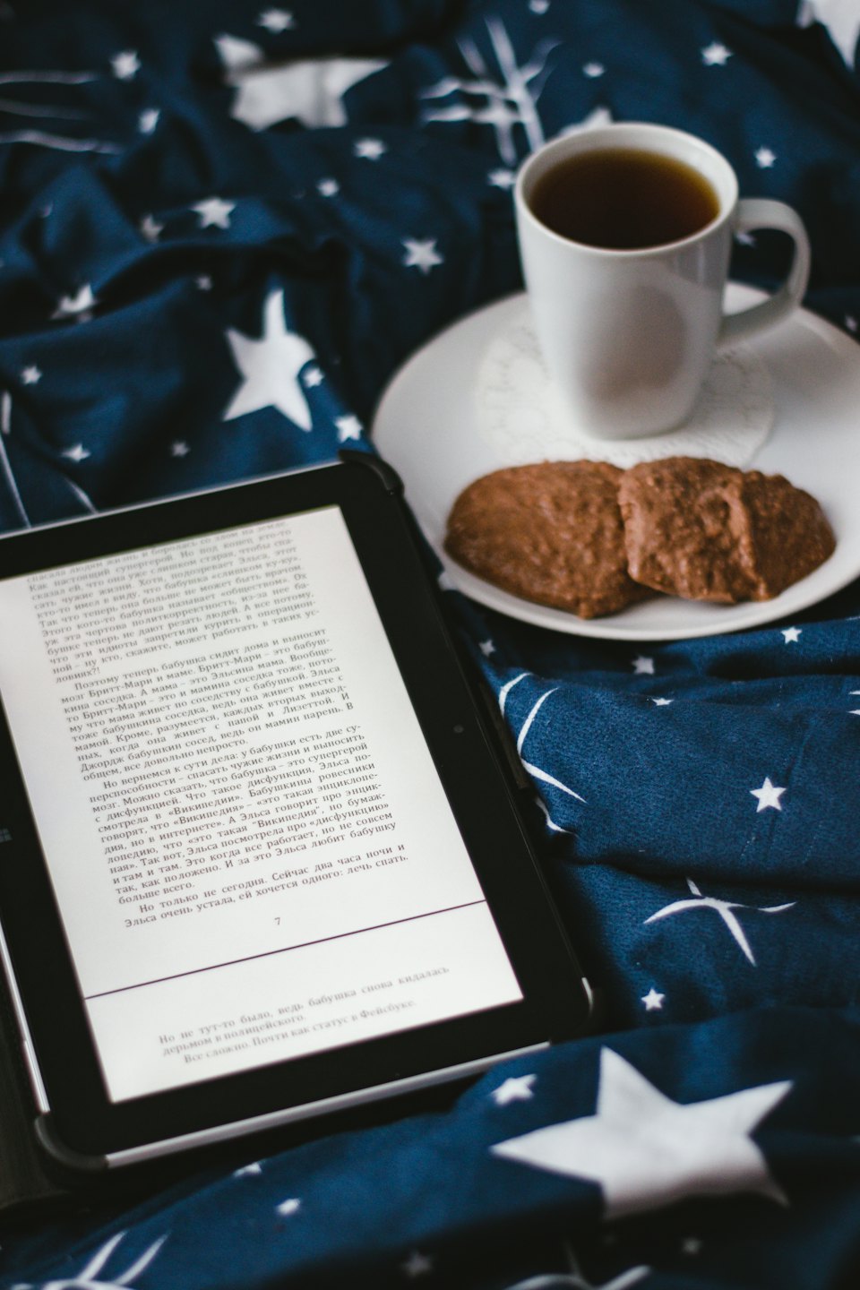 Ein E-Reader, Tee und Kekse auf einer Sternendecke.